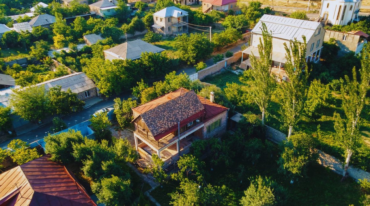 Aerial view of the stone house with red roof among mature trees in Yeghvard
