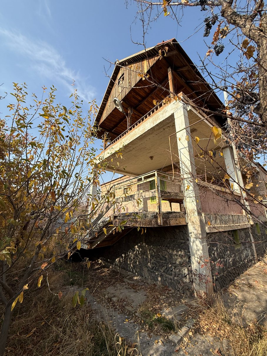 Stone house exterior seen from below the plot, current condition